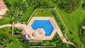 Eine Vogelperspektive auf einen Pool in Sechseckform, umgeben von einem gepflegten Rasen und Bäumen.