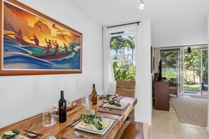 Ein Essbereich mit Tisch für zwei Personen, einem Bild über dem Tisch und Blick ins Freie durch ein Fenster.