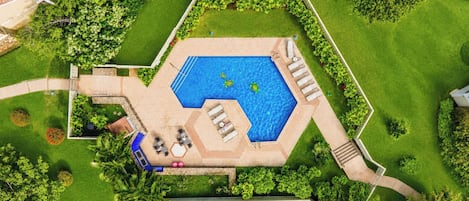 An aerial view of a swimming pool with a hexagonal shape, surrounded by a well-maintained lawn and trees.