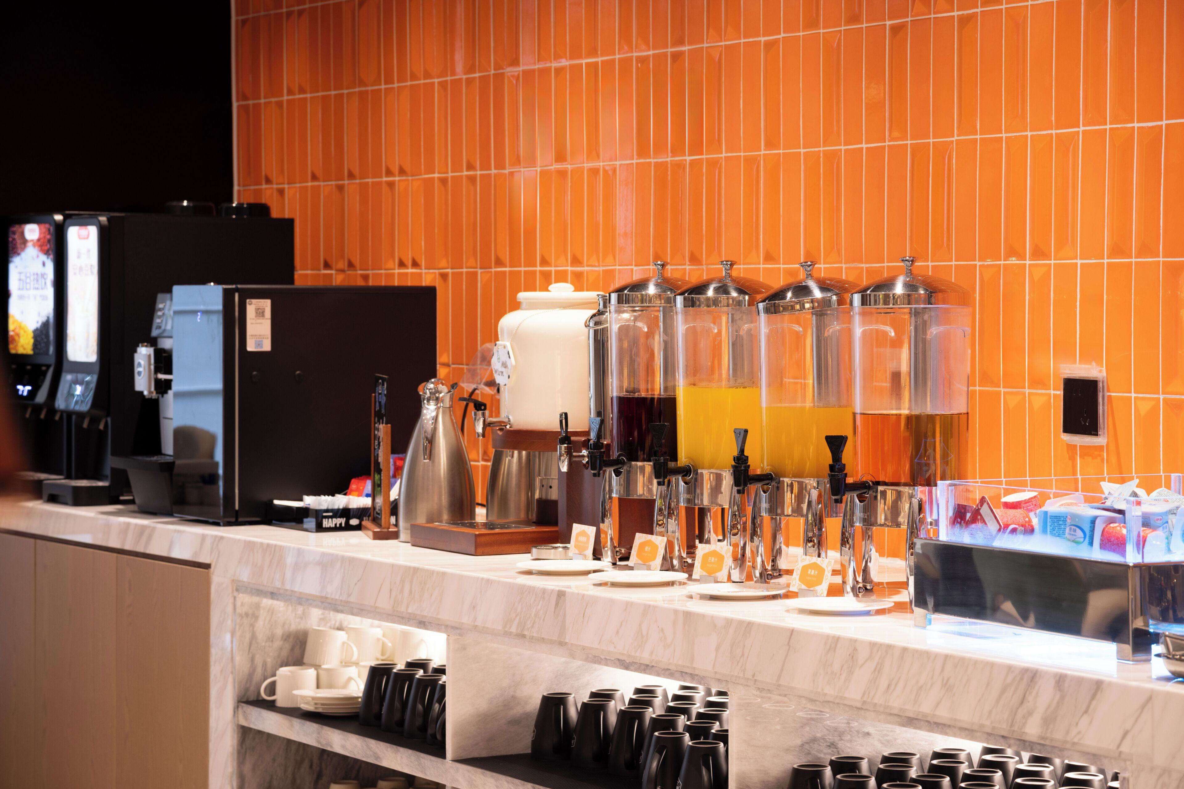 Uma estação de café com dosadores, uma máquina de café e um refrigerador.