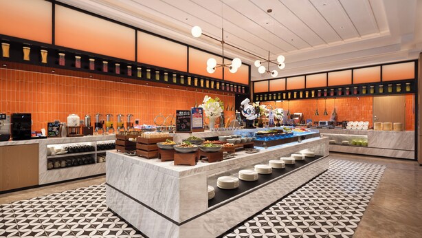 A modern hotel lobby with a central buffet area, marble flooring, and a patterned tile design.