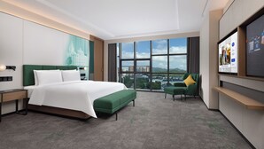 A modern hotel room with a large bed, a green sofa, a TV, and a city view.