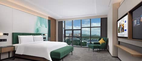 Habitación de hotel moderna con una cama grande, un sofá verde, un televisor y vistas a la ciudad.