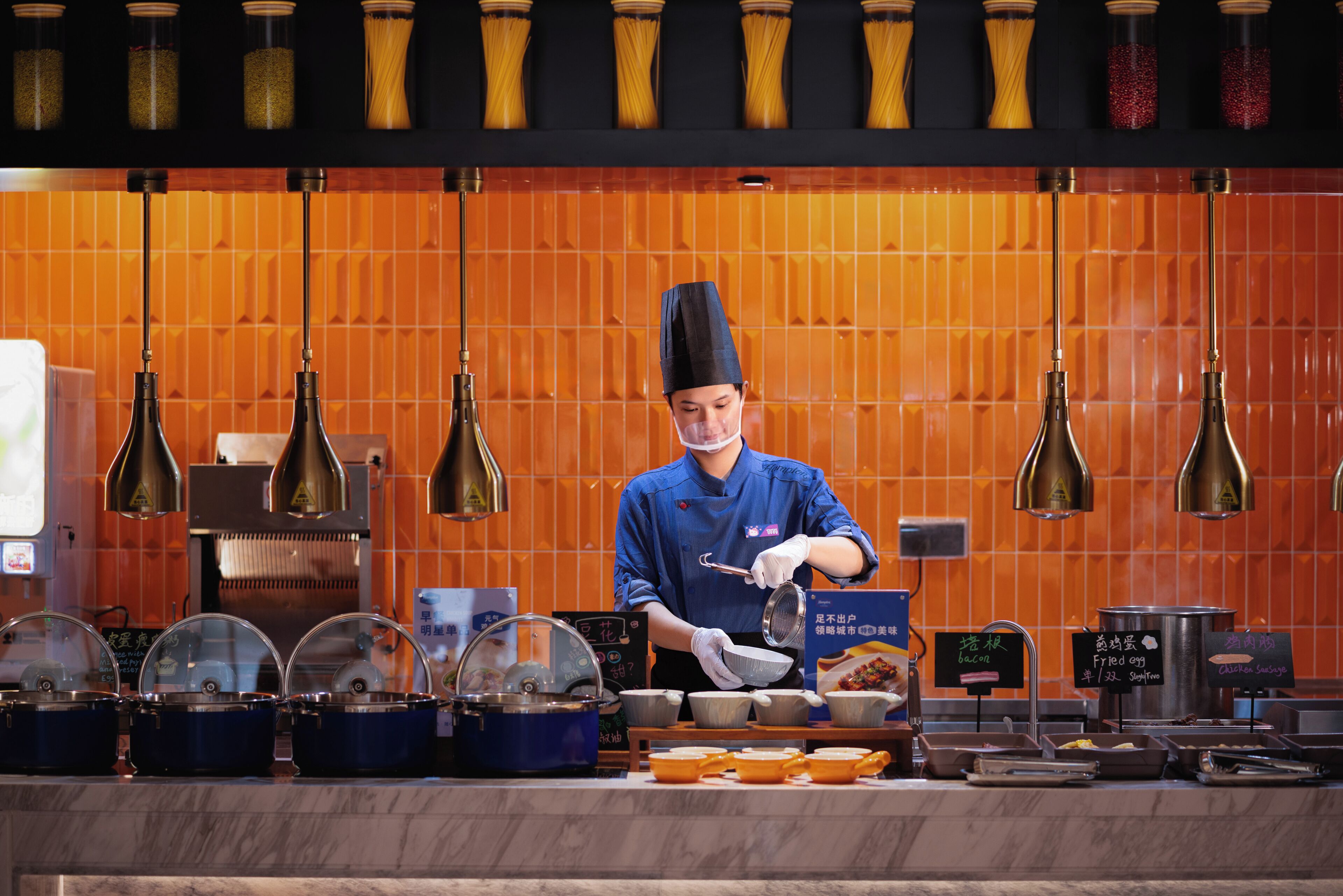 Uma pessoa vestindo uniforme azul preparando comida em um balcão, com diversos utensílios de cozinha e ingredientes.