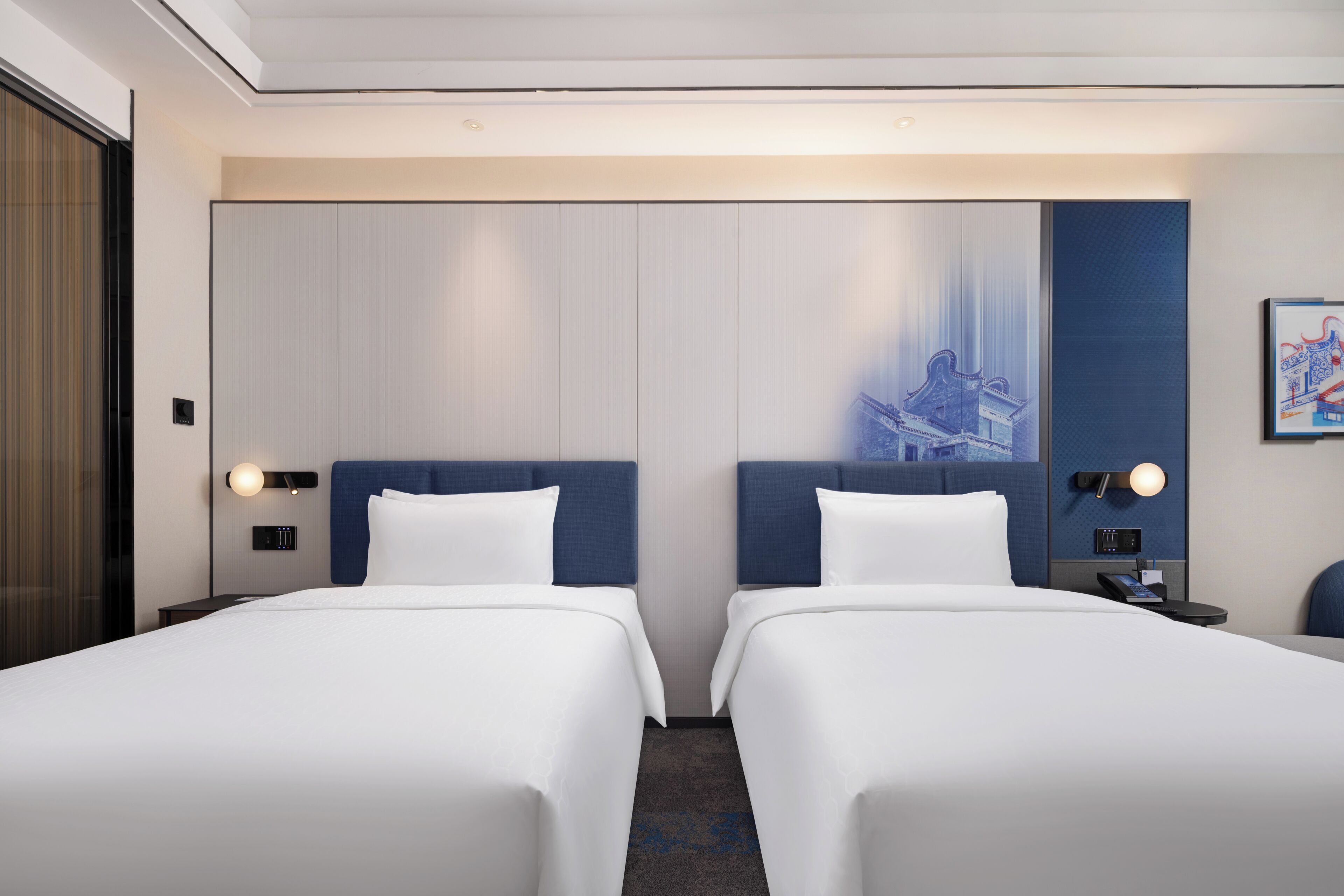 A hotel room with two beds, a large wall mural, bedside tables with lamps, and a door with a view.