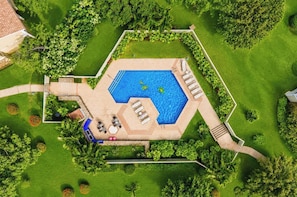 Eine Vogelperspektive auf einen Pool in Sechseckform, umgeben von einem gepflegten Rasen und Bäumen.