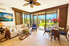 A spacious living room with a sofa, coffee table, and chairs, large windows with a view of greenery, and a ceiling fan. - Napili Point | Oceanfront 2 BR, Sleeps 8 | Car Incl. w/ 6+ Nights | NAP ML-4154 KBM (Lahaina)