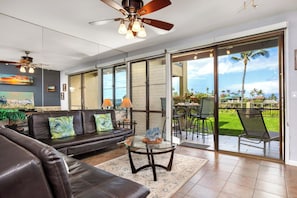 A modern living room with a leather sofa, a glass coffee table, and a ceiling fan. - Napili Point | Oceanfront 2 BR, Sleeps 8 | Car Incl. w/ 6+ Nights | NAP ML-4154 KBM (Lahaina)