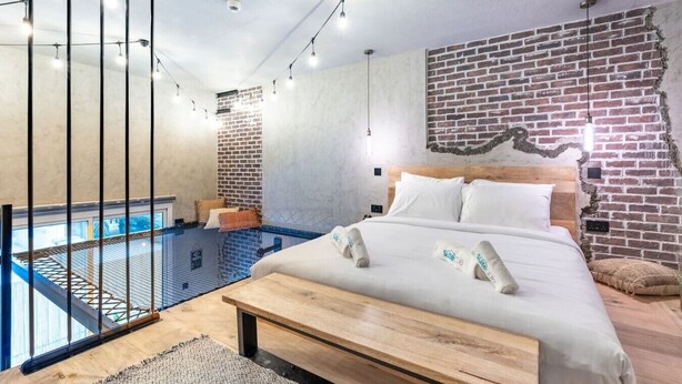 Ein modernes Schlafzimmer mit Backsteinwand, einem hölzernen Bett und Blick auf ein Hallenbad.