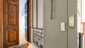 Une porte en bois, un portail en métal, un interrupteur et une petite fenêtre sur un mur gris.