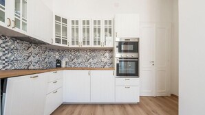 Une cuisine avec des meubles blancs, un pare-feu en carrelage et un plan de travail en bois.
