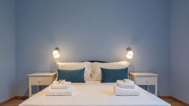 Un lit double avec deux tables de chevet, chacune équipée d’une lampe, et des serviettes sur le lit.