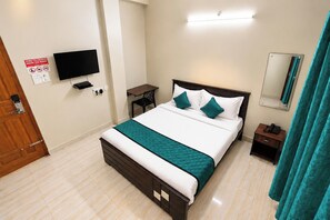 Habitación de hotel con cama, escritorio, silla, televisor, teléfono y espejo.