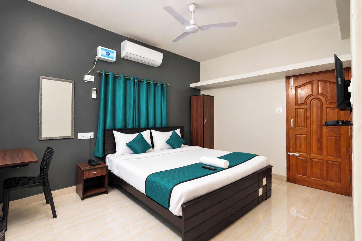 A hotel room with a bed, a desk, a chair, a wardrobe, a television, and a ceiling fan.