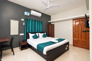 Habitación de hotel con cama, escritorio, silla, armario, televisor y ventilador de techo.