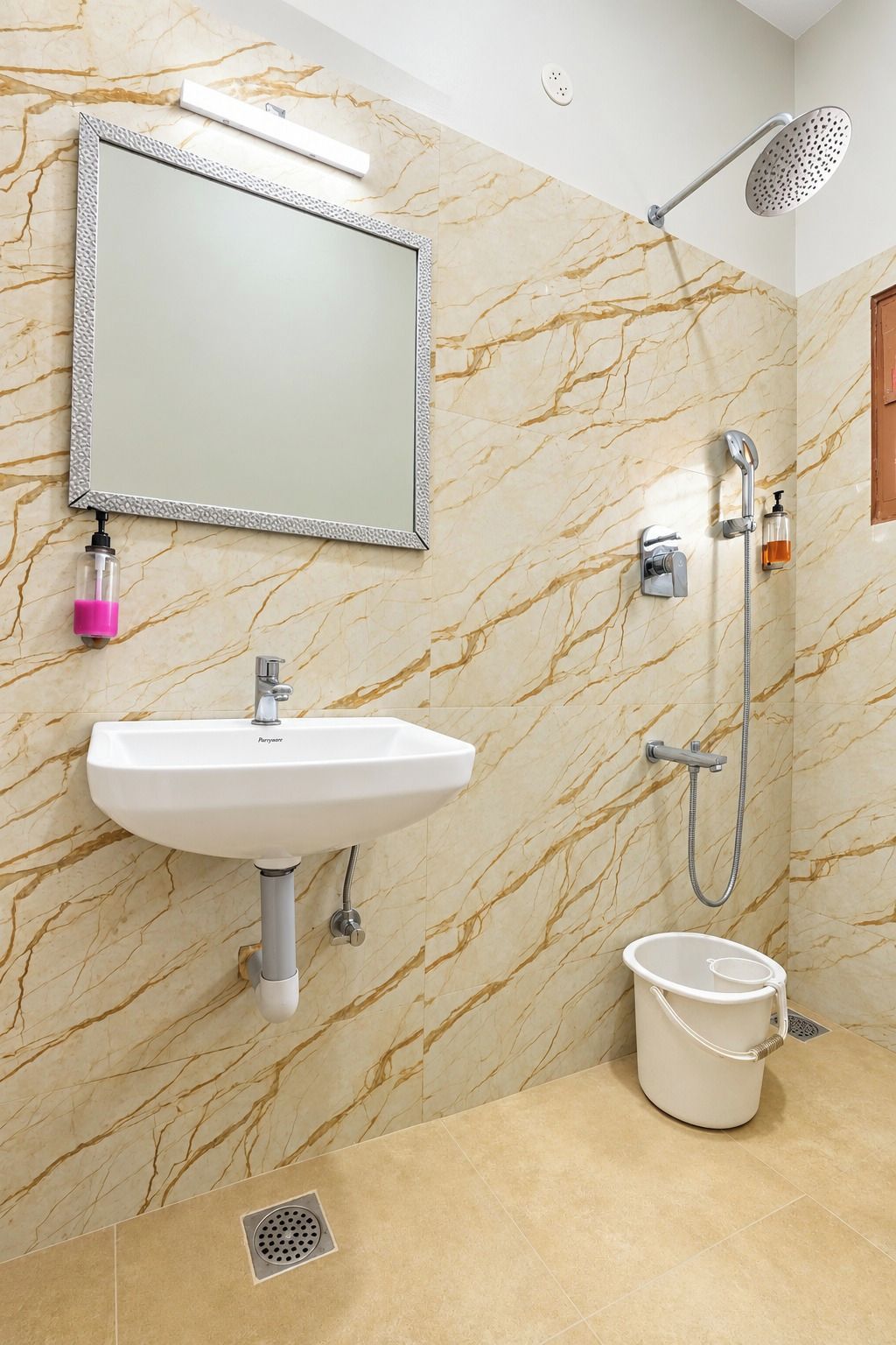 A bathroom with a marble wall, a sink, a mirror, a shower, and a bucket.