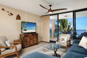 A living room with a TV, wooden furniture, a glass coffee table, and a view of the ocean. - Mahana Villas | Oceanfront 5 BR Sleeps 16 | Car Incl. w/ 6+ Nights | MAH ML-4166 by KBM (Lahaina)