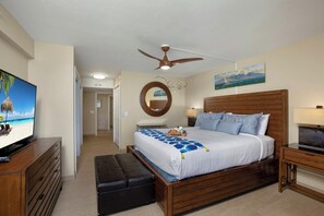 A bedroom with a bed, a television, a ceiling fan, a wooden headboard, a bedside table, and a nightstand. - Mahana Villas | Oceanfront 5 BR Sleeps 13 | Car Incl. w/ 6+ Nights | MAH ML-4169 by KBM (Lahaina)