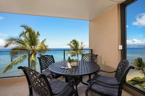 A balcony with a round table and chairs, a view of the ocean, and palm trees. - Mahana Villas | Oceanfront 5 BR Sleeps 13 | Car Incl. w/ 6+ Nights | MAH ML-4169 by KBM (Lahaina)