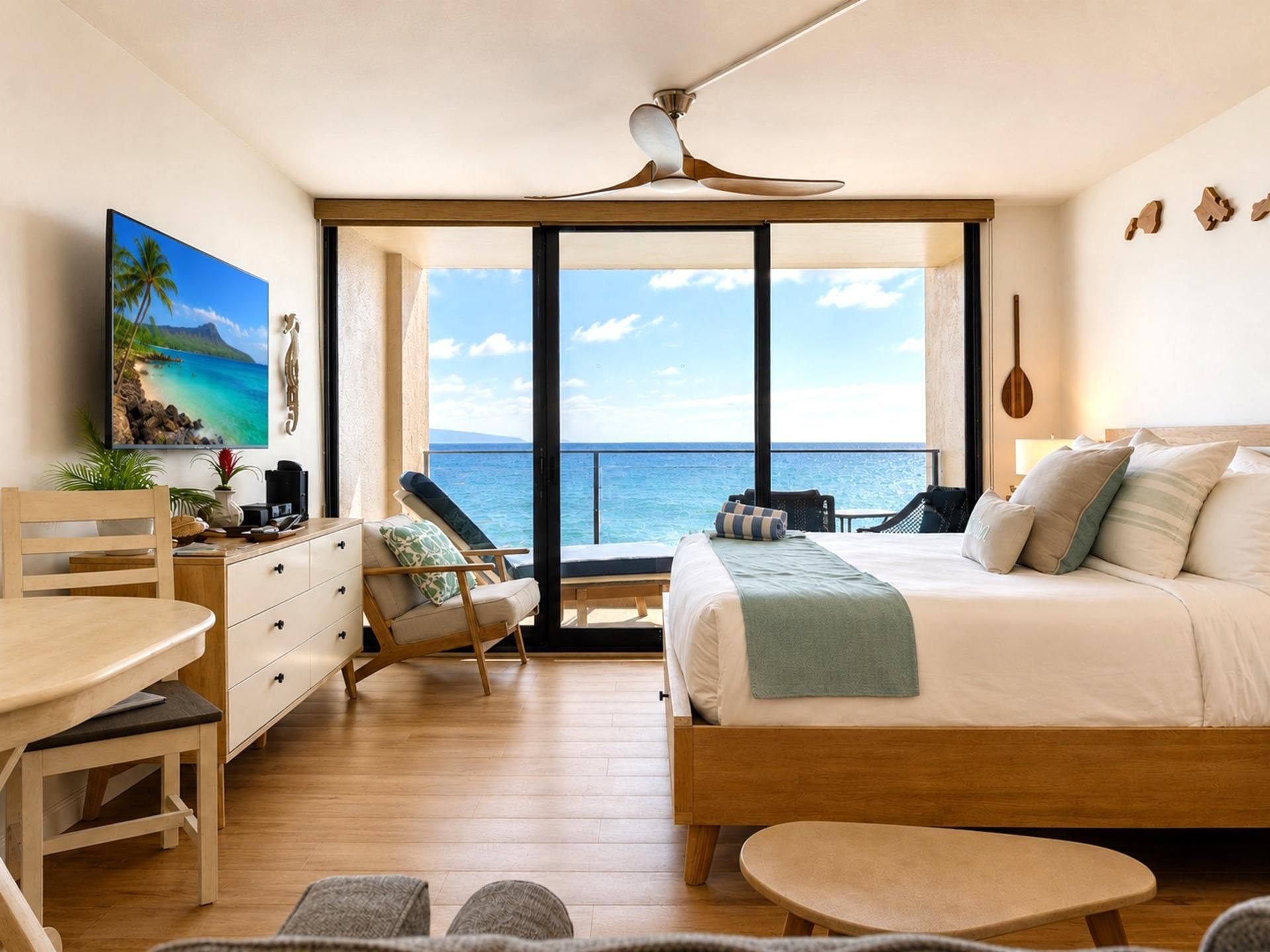 A bedroom with a large bed, a desk, a chair, a small table, and a view of the ocean.