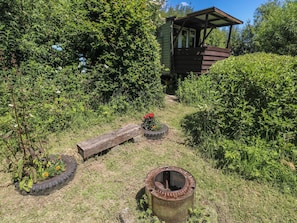 A rustic outdoor area with a wooden structure, tire planters with flowers, and a metal barrel.