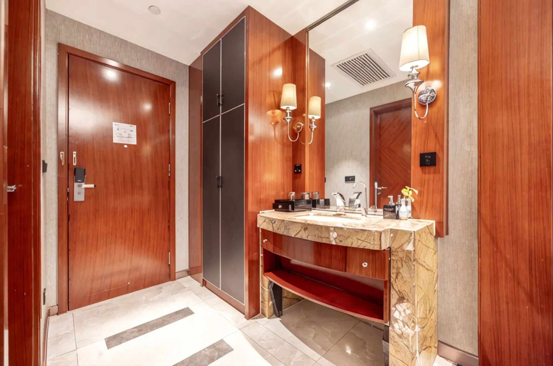 A hotel bathroom with a wooden vanity, a mirror, and wall-mounted lights.