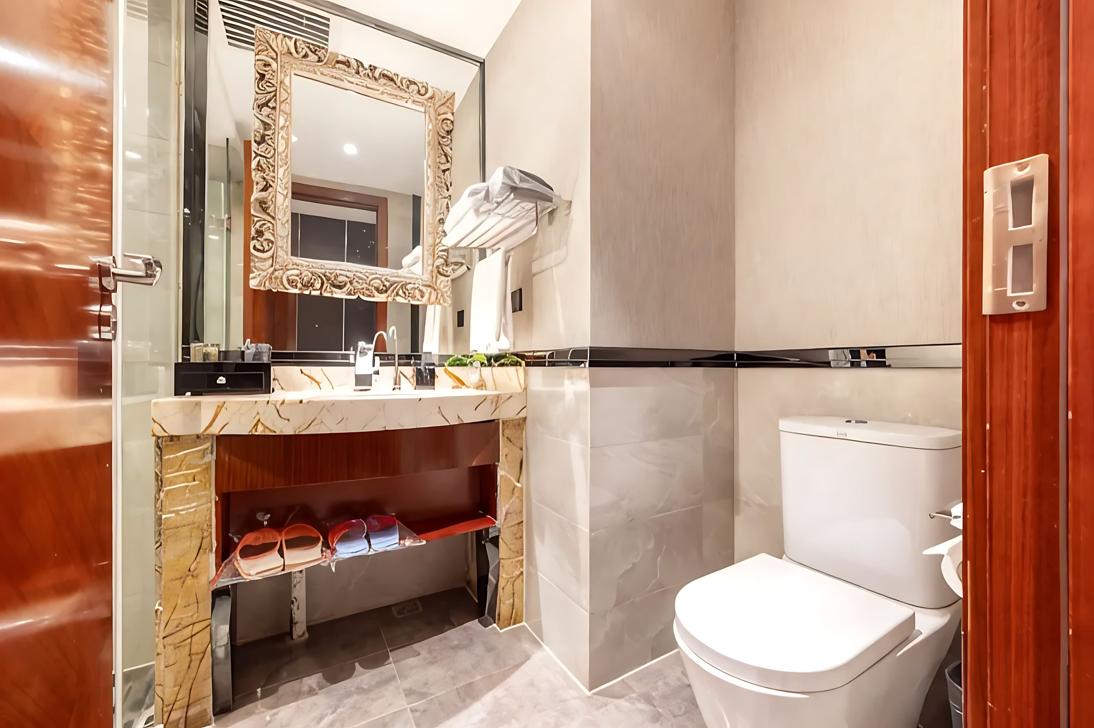 A bathroom with a marble vanity, a toilet, and a large mirror with an ornate frame.