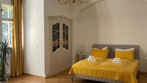 Un dormitorio con cama, armario, candelabro y ventana con cortinas.