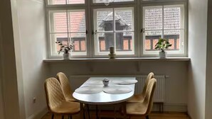 Un comedor con una mesa redonda y cuatro sillas, una ventana con vistas a un edificio y un radiador debajo de la ventana.