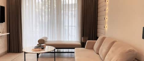 A modern living room with a sofa, a round table, and a large window with curtains.