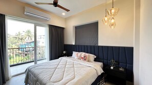 A bedroom with a bed, a ceiling fan, an air conditioning unit, a nightstand, and a view of the outside. - Calangute Heights (Calangute)