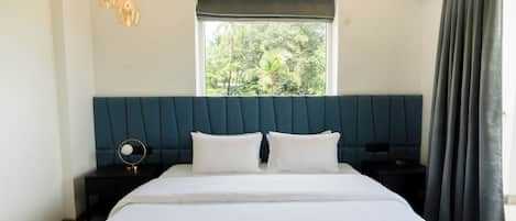 A bedroom with a large bed, two bedside tables, a window with a view of greenery, and a curtain.