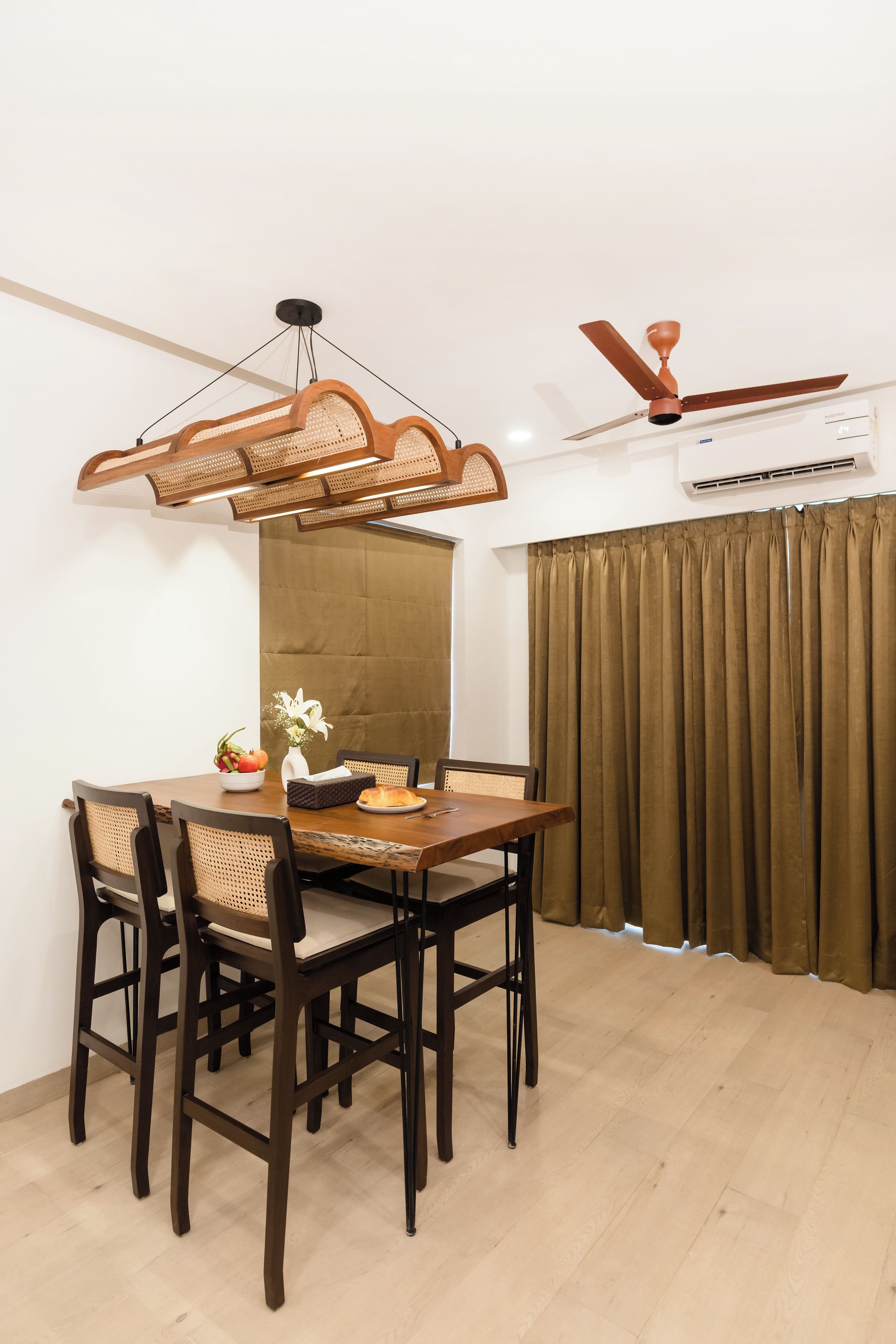 Uma sala de jantar com uma mesa de madeira, quatro cadeiras, um vaso com flores e um ventilador de teto.