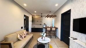 Una sala de estar moderna con un sofá, una mesa de comedor, sillas, un televisor y una cocina al fondo.
