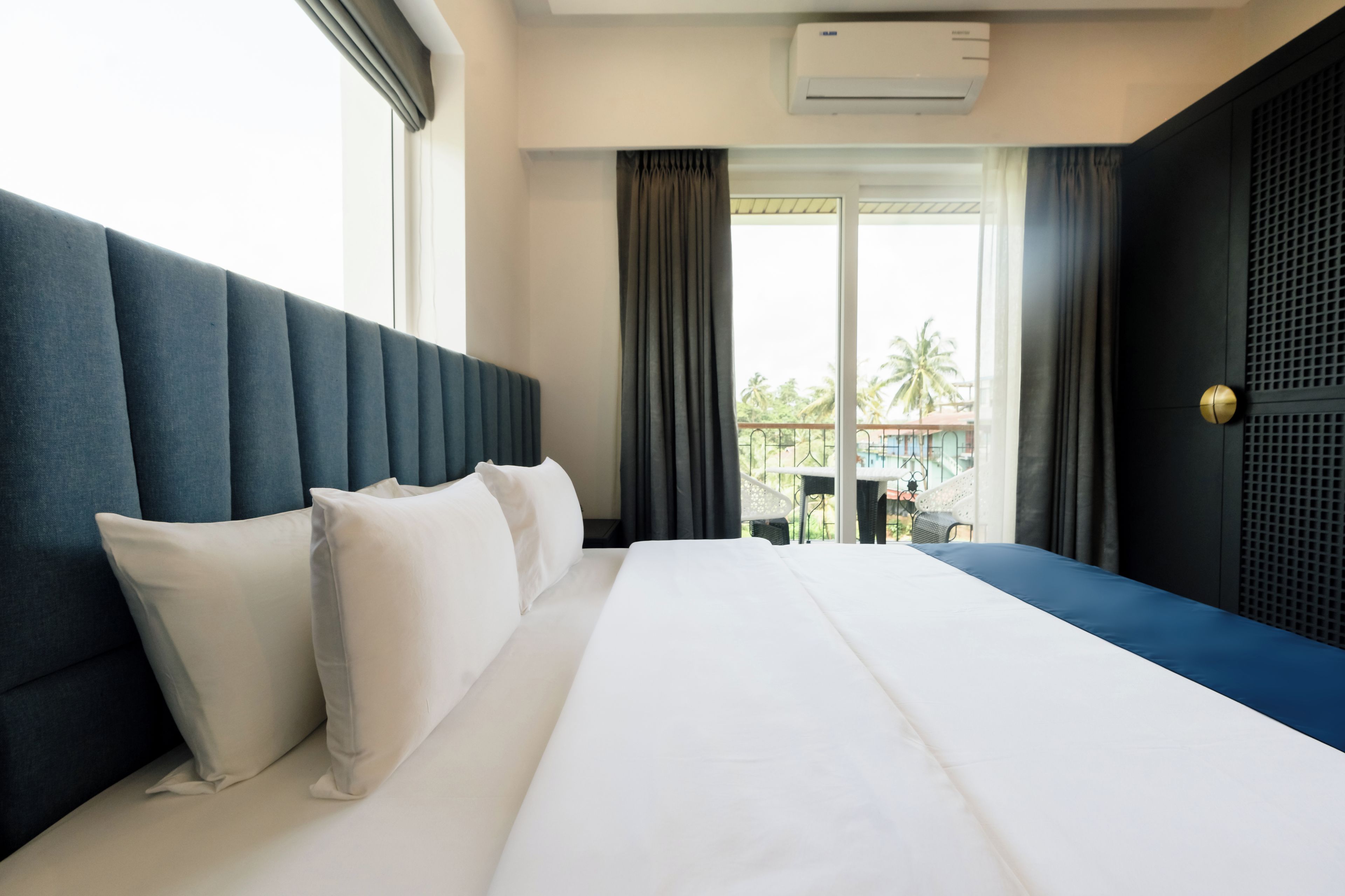 Ein Hotelzimmer mit einem großen Bett, einem Kopfteil, einem Fenster mit Vorhängen und einer Klimaanlage.