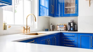 Une cuisine avec des meubles bleus, un plan de travail blanc, un robinet doré et une machine à café.