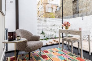 A cozy corner with a patterned armchair, a small round table with a candle, and a white table with a vase of flowers. - Modern Classic in Angel, by Veeve (London)