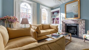 Un salon avec un canapé beige, une table basse en verre, une cheminée et un grand miroir.
