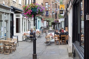 A street with outdoor seating, a sign for 'KIPFERL,' and a hanging flower basket. - Modern Classic in Angel, by Veeve (London)