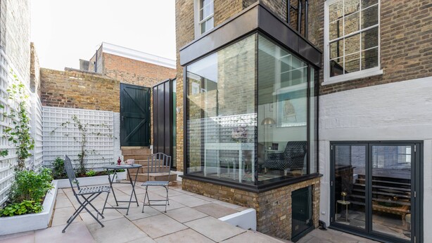 Une terrasse moderne avec une structure en verre, des sièges d’extérieur et un mur en briques.