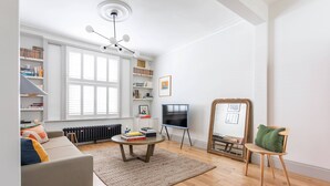 Un salon comprenant un canapé, une table basse, un fauteuil, une bibliothèque, un téléviseur et un radiateur.