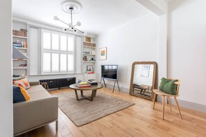 Ein Wohnzimmer mit einer Couch, einem Couchtisch, einem Sessel, einem Bücherregal, einem Fernseher und einer Heizung.