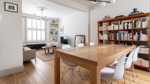 Un salon moderne avec une table à manger en bois, des chaises blanches, une bibliothèque et un téléviseur.