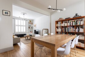 Ein modernes Wohnzimmer mit einem Holzesstisch, weißen Stühlen, einem Bücherregal und einem Fernseher.