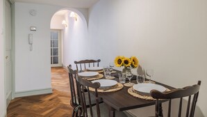 Comedor con mesa de madera oscura dispuesta para cuatro personas, platos blancos y un jarrón con girasoles.