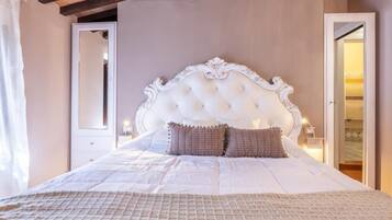 Un dormitorio con cabecera capitonada, una cama grande con colcha acolchada, un espejo y una mesita de noche con lámpara.