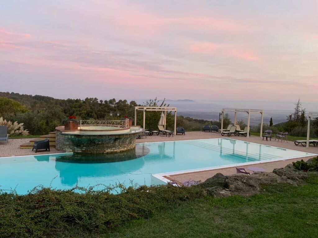 A swimming pool with lounge chairs and a gazebo, surrounded by greenery and hills.