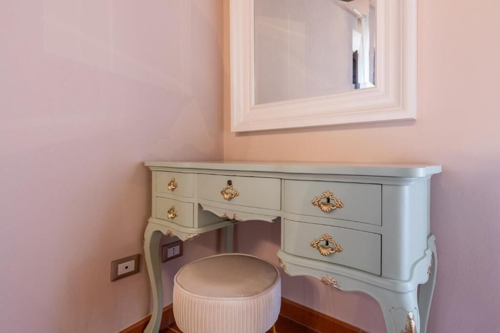 Une coiffeuse bleu clair agrémentée de poignées dorées décoratives, un miroir au-dessus et un tabouret rond blanc.