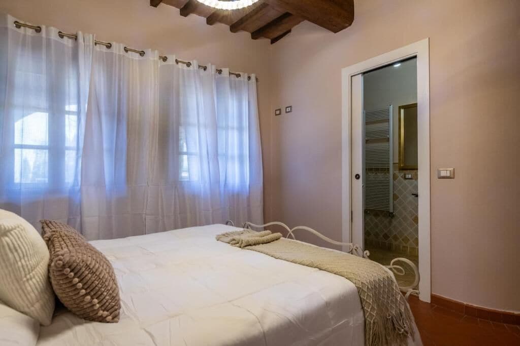 A bedroom with a bed, curtains, a door, and a view of a tiled bathroom.