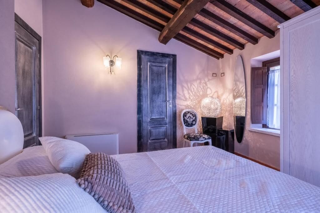 A bedroom with a bed, a chair, a door, and a wall-mounted light fixture.